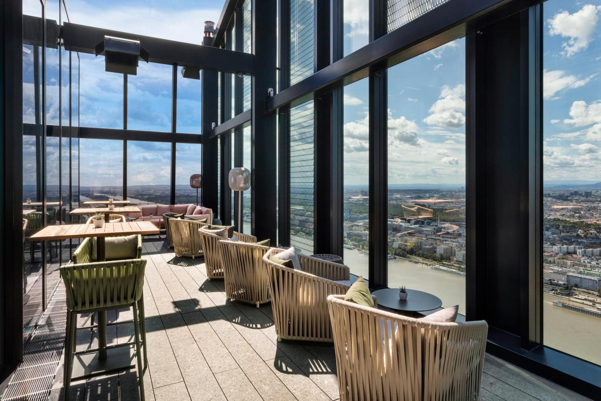 Melia Vienna Hotel Exterior photo The image shows a stylish indoor space with large floor-to-ceiling windows that provide a panoramic view of the landscape outside. The area features several comfortable seating arrangements, including modern chairs and small tables. The design is sle
